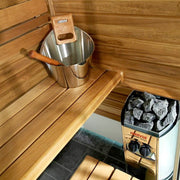 Wooden sauna interior with metal bucket, wooden ladle, and Harvia stove.
