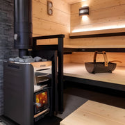 Wood-fired stove in a wooden sauna with benches and a basket.