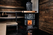 Wood-burning sauna heater in a rustic sauna setting with wooden walls and floor.